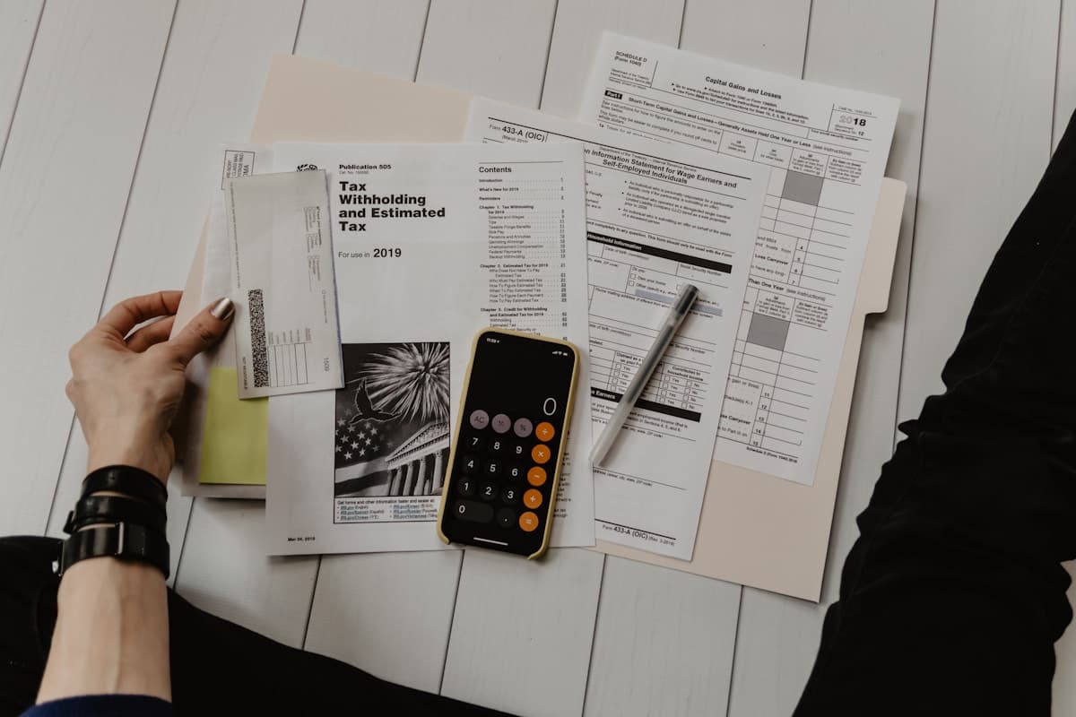Calculator and financial documents on a desk beside a laptop showing a website project